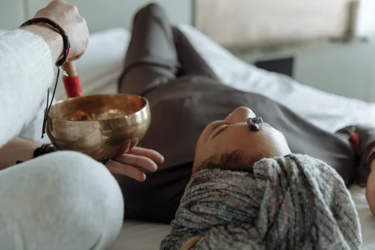A singing bowl held above someone resting, with an amethyst on the forehead